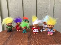 Side view of nine vintage troll dolls arranged in two rows on wooden surface showing colorful hair and outfits