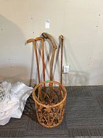 Four carved wood walking sticks and bamboo basket against a wall