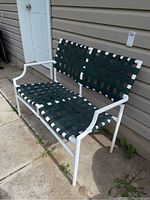 Metal framed outdoor bench painted white with green woven webbing seat and backrest, placed on concrete patio.