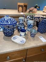 Overview of all ceramic kitchenware including turtle dish, mugs, beer stein, urn, teapot, and trays arranged on counter.