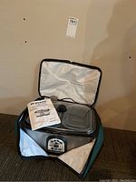 Slow cooker inside open teal insulated carrying bag with digital panel visible and owner's manual resting on top.