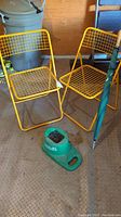 Two yellow metal mesh folding chairs, green Denali Clubtub in front, large green rain umbrella standing upright behind chairs