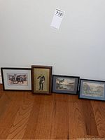 Four diverse framed prints leaning against a white wall on wooden floor: charging horses, soldier in uniform, and two landscapes