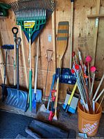 Photo of various garden tools and outdoor equipment including shovels, rakes, wooden oar, and stake bucket