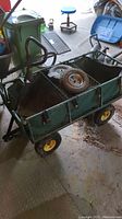 Metal garden wagon with green canvas insert, grated metal body, plywood bottom, detachable handle and two spare wheels inside.