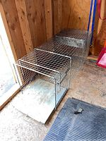 Side and perspective view of the metal live trap showing its rectangular shape, wire mesh construction, and front entry flap door.