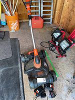 Black & Decker battery powered lawn mower with rechargeable battery and charger on a concrete floor next to some other equipment.