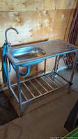 Front-left view of entire sink assembly including basin, drainboard, frame and hoses