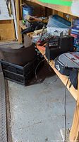 Garage corner with small totes, thick chain on floor, grinding wheel box, various items on shelf near Husky storage seat