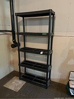 Full view of black resin shelving unit with five shelves against unfinished wall