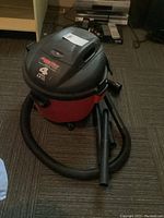 Overview of Aqua Vac Shop Vac wet/dry vacuum, red and black, showing vacuum body, hose, and attachments on floor.