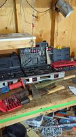 Overview of multiple tool sets in black and red plastic cases on a wood workbench, along with a level, two axes, and branch trimmer