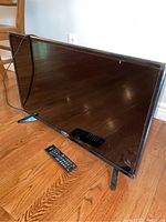 Photo of the Toshiba flat screen TV on wooden floor with its remote placed in front.