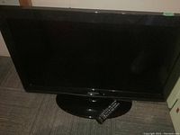 32 inch Samsung TV on black stand with remote control placed on pedestal base, TV screen powered off