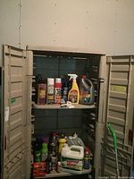 Front view of open Suncast resin utility cabinet showing two shelves with various cleaning and maintenance products inside.