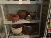 Gray plastic utility shelving unit with slatted shelves holding various pots. Shelving dimensions approximately 36x14x55 inches.