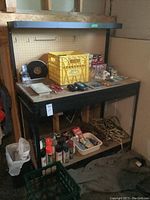 Front view of the workbench showing the metal frame, MDF top, yellow crate with miscellaneous items on top, peg board on back, and items stored underneath.