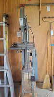 Full side view of the Rockwell/Beaver band saw showing the vertical posture on metal legs, power cord, adjustment knobs, and cutting table.