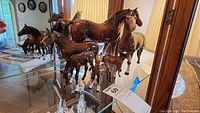 Lot of six brown and cream Beswick horse figurines on glass shelf showing various sizes and poses.