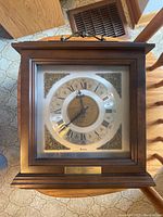 Front view of the Bulova wall clock showing the wood frame, glass front, and decorative clock face with embossed tractor motif.