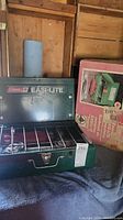 Green Coleman Easi-Lite camp stove with two burners and metal grill, displayed open with original box standing beside it.