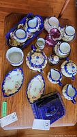 Top view showing multiple pieces of vintage unsigned porcelain china with floral designs and cobalt blue borders arranged on a wooden surface.