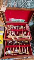 Wooden cutlery box interior showing red fabric lining and multiple cutlery pieces organized in two layers with forks, spoons, and knives.