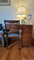 Front view of vintage wooden desk with four drawers and chair with lyre backrest under desk surface, showing upholstery wear on chair seat.