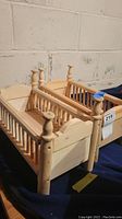 Two unfinished wooden doll beds side by side with turned bedposts and slatted sides.