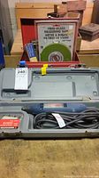 Ryobi rotary tool kit closed case with fiberglass measuring tape and wooden boxes of hand tools in background