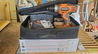 Ridgid cordless drill, charger, and battery in black soft carrying case on a wooden surface.