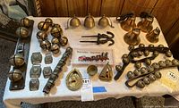 Full overview of lot on white cloth showing different sizes and styles of brass horse bells, several brass medallions, and brass door knocker.