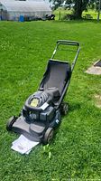 Full view of Yardworks lawn mower on grass with grass catcher attached and manuals positioned near front wheel.