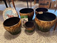 Overview of five ceramic plant pots with brown to green glaze, arranged on carpet floor, with horse themed thermometer visible in the background.