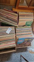Four cardboard boxes filled with vintage vinyl records, showing some visible album covers including country western and Christmas themes. Records vary in color and cover art for 70's singer-songwriter and oldies genre.
