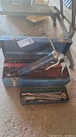 Overall view of toolbox with grease gun, sockets, wrenches, and ratchets inside.
