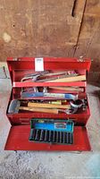 Red metal toolbox with variety of hand tools inside and blue impact socket set visible.