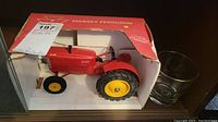 Photo of 1/16 scale Massey Ferguson tractor model in original red box and classic car glass tumbler to the right