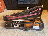 Violin with bow inside open hard case showing case interior and violin details.