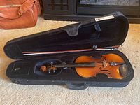 Open black hard case containing wooden violin and bow, showing overall lot contents.