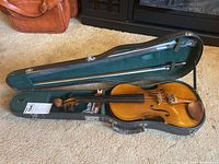 Violin inside open hard case with bow placed above the violin, showing full length and condition.