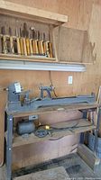 Full view of lathe on stand with wall-mounted rack of chisels above