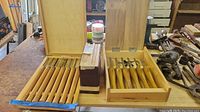Two hinged wooden chisel boxes open side by side on a workbench with a stack of Shop Notes booklets between them
