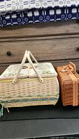 Side angle view showing both sewing baskets: larger basket with floral tapestry lid and fabric handles, smaller brown basket with single handle