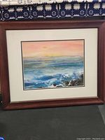 Frontal photo of framed beach painting showing ocean waves under colorful sky, signed by Carol Hart.