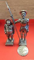 Front view of Don Quixote and Sancho Panza metal figurines with coin for scale.