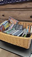 Overall view of a basket filled with used DVDs showing variety of movies and cases.