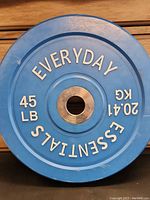 Blue Everyday Essentials 45lb bumper plate lying on wooden surface showing front face.