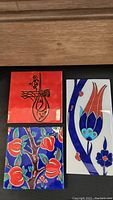 Three handmade Iznik ceramic tiles displayed on a wooden surface, showing unique traditional designs with vibrant colors.
