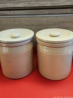 Two beige vintage ceramic canisters with lids standing side by side, both marked with the number 2. Both in good condition.
